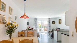 Een eetruimte met een tafel en stoelen, een bloevas en een keuken op de achtergrond.