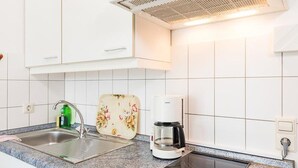 Une cuisine avec des meubles blancs, un évier, une machine à café et une plaque de cuisson à induction.