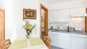 Une cuisine de taille réduite avec des meubles blancs, une table à manger recouverte d’une nappe à motifs floraux et un vase rempli de fleurs jaunes.