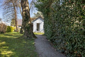 A gravel path leading to a white building with a sloped roof, surrounded by trees and greenery.