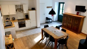 Una cocina moderna con armarios blancos, una mesa de comedor con sillas, un televisor montado en la pared y un mueble de madera.
