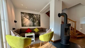 Una sala de estar con un sofá, dos sillones verdes, una mesa de centro, un cuadro, una chimenea y una escalera.