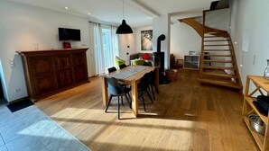 Amplia sala de estar con una mesa de comedor de madera, sillas, un televisor montado en un mueble, una escalera y un ventanal grande.