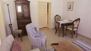A living room with a sofa, armchair, dining table with chairs, a cabinet, and a remote control on a coffee table. - Holiday Home 'Marienblick' with Private Terrace, Private Garden and Wi-Fi (Beeskow)