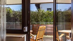 Une pièce dotée d’une porte-fenêtre coulissante qui donne sur un patio extérieur aménagé avec une chaise en bois et une petite table.