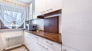 Une cuisine avec des meubles blancs, un plan de travail en bois, une machine à café et une fenêtre ornée de rideaux légers.