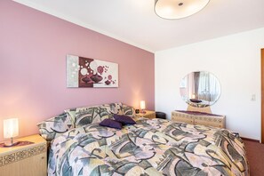 Un dormitorio con una colcha estampada, un espejo decorativo y una obra de arte en la pared.