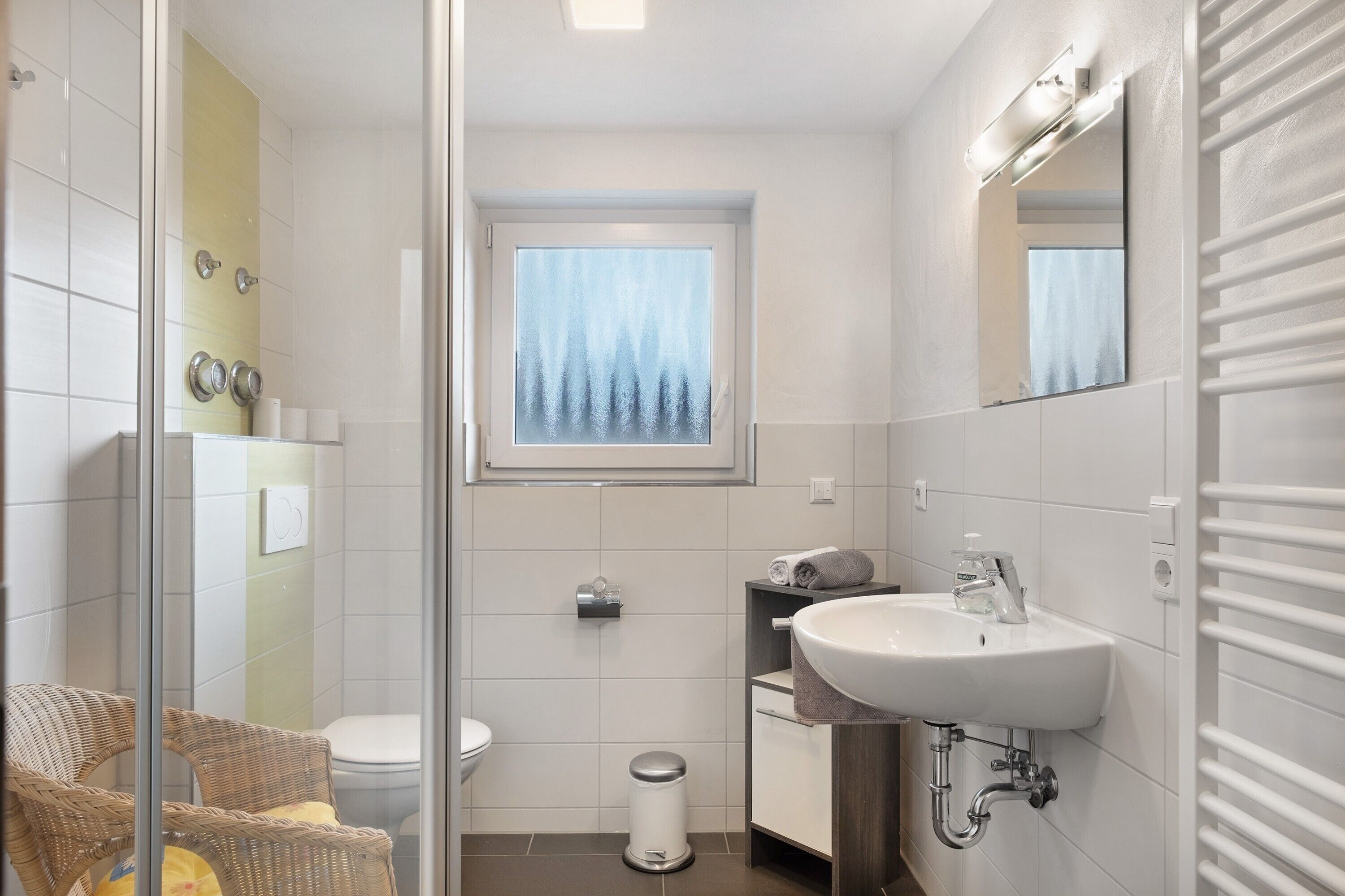 Une salle de bain avec une douche à parois de verre, des toilettes, un lavabo avec un miroir et une fenêtre donnant sur les arbres.