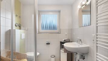 Une salle de bain avec une douche à parois de verre, des toilettes, un lavabo avec un miroir et une fenêtre donnant sur les arbres.