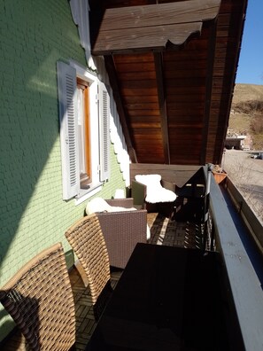 A wooden deck with wicker furniture, a window with shutters, and a staircase leading to a covered area.
