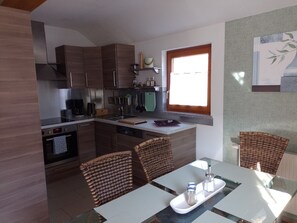 A compact kitchen with modern appliances, a dining area with wicker chairs, and a window providing natural light.