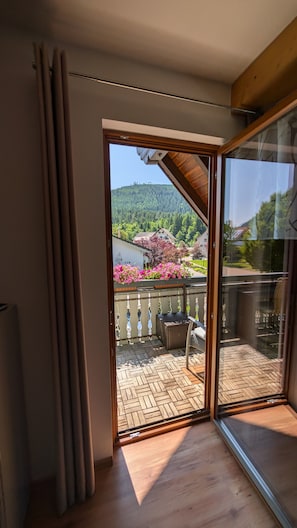 Una habitación con puerta de vidrio corredera que da a un balcón exterior con suelo de espiga y mobiliario de mimbre.