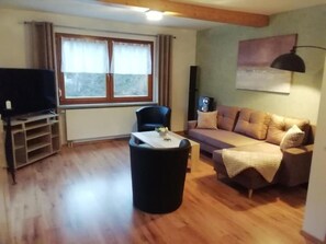Una sala de estar con sofá, una mesa de centro, televisor, lámpara y ventana con cortinas.