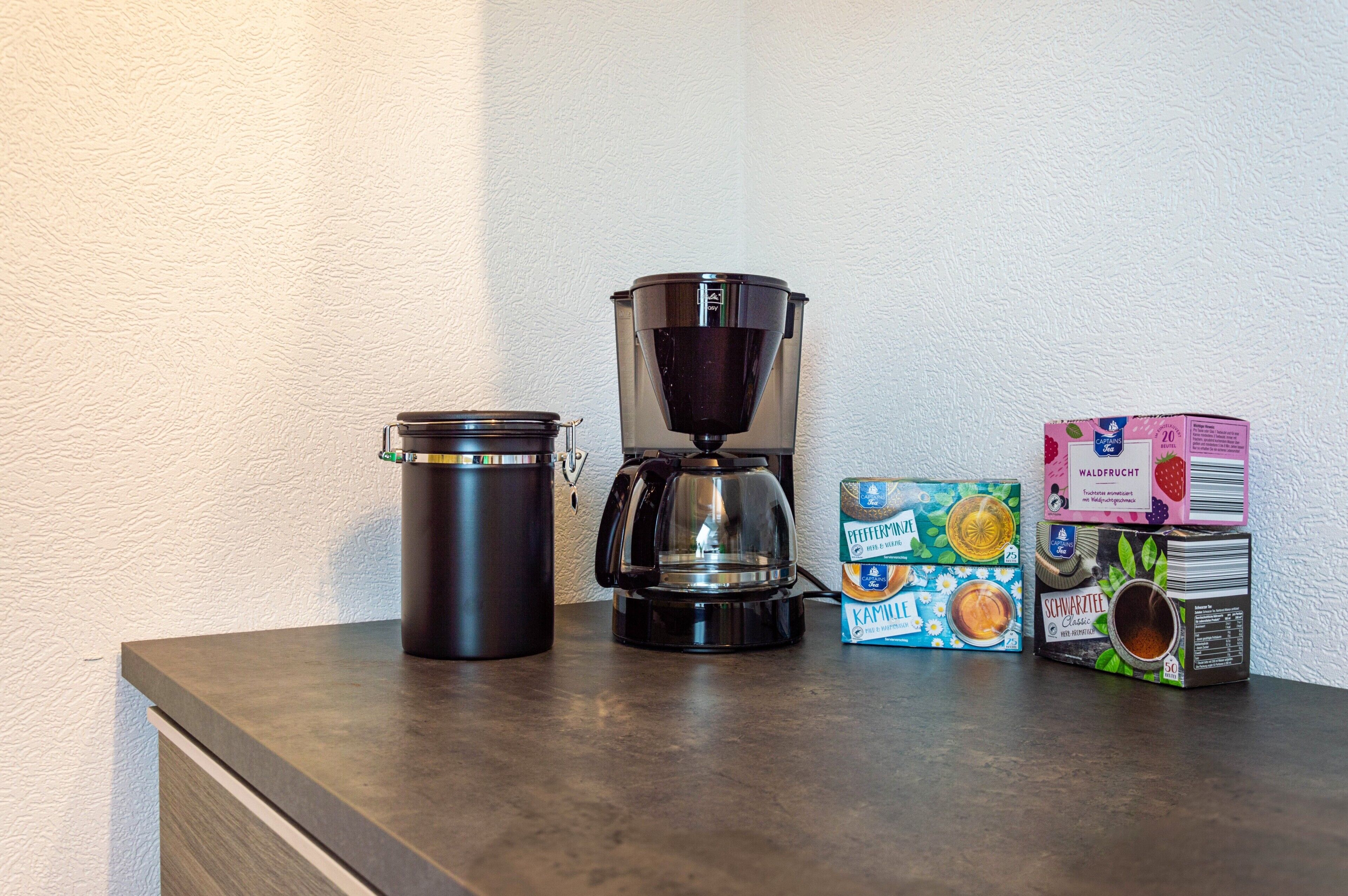 A coffee maker, a thermos, and boxes of coffee on a countertop.