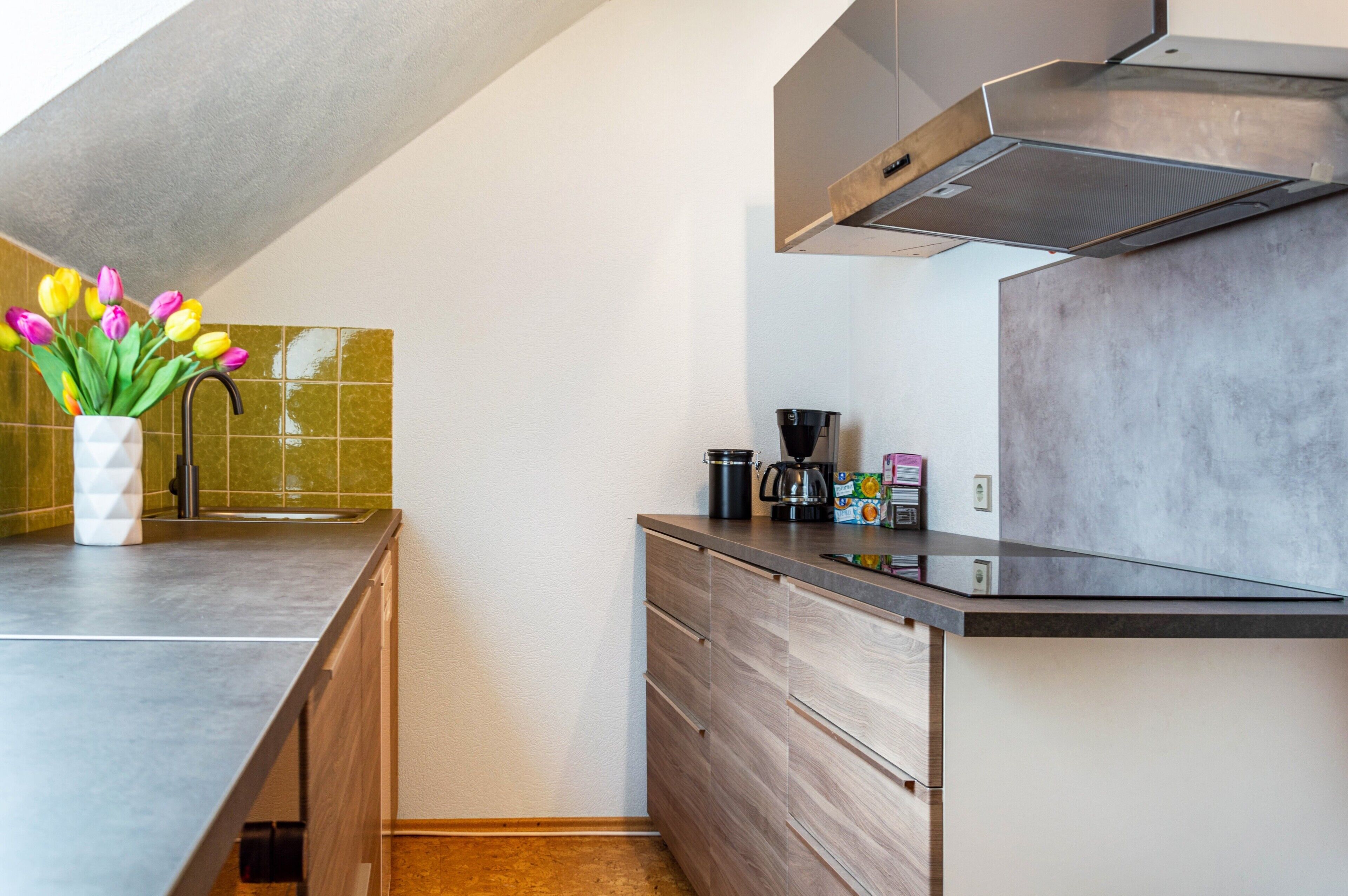 A modern kitchen with a built-in stove, a coffee maker, and a vase with tulips on the counter.