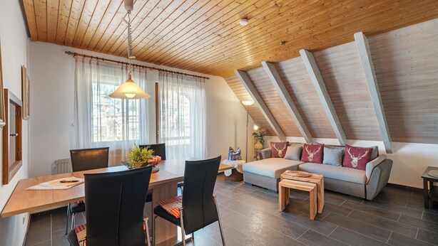 A modern loft-style room with a dining area, a sofa, and a wooden ceiling. - Apartment 'Karin' with Lake View and Balcony (Schonach)