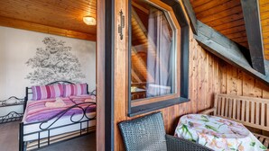 A wooden interior with a bed, a wicker chair, a table with a floral tablecloth, and a window with curtains. - Apartment 'Karin' with Lake View and Balcony (Schonach)