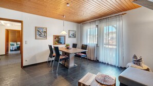 A modern dining area with a wooden ceiling, a dining table with chairs, a sofa, and a window with curtains. - Apartment 'Karin' with Lake View and Balcony (Schonach)