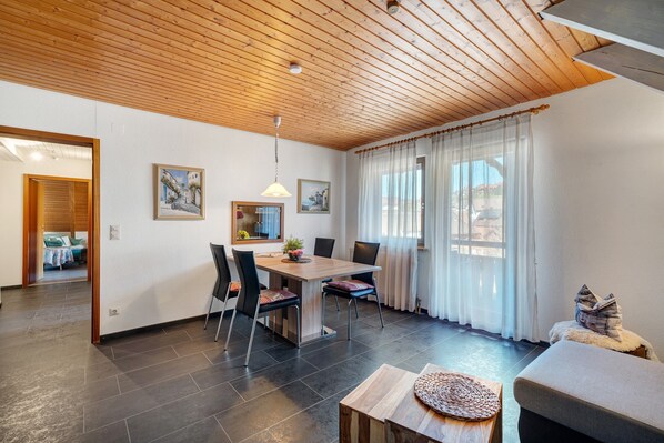 Un espace de repas moderne avec un plafond en bois, une table à manger avec des chaises, un canapé et une fenêtre avec des rideaux.