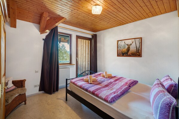 A bedroom with a bed, a window, a door, a chair, and a painting on the wall.