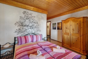 Une chambre à coucher avec un lit, une armoire en bois et un mur décoré d’une fresque représentant un arbre.