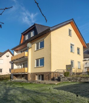 Ein zweistöckiges Wohngebäude mit Balkon, Satellitenschüssel und kleinem Garten.