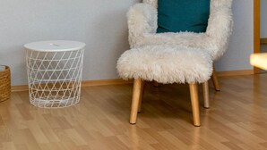 Una habitación con una silla mullida, una cesta blanca de metal y una obra de arte en la pared.