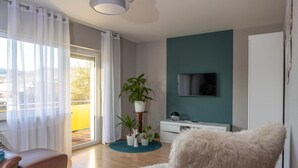 Una sala de estar moderna con un sofá, un sillón mullido, un televisor montado en la pared y un arreglo de plantas en macetas.