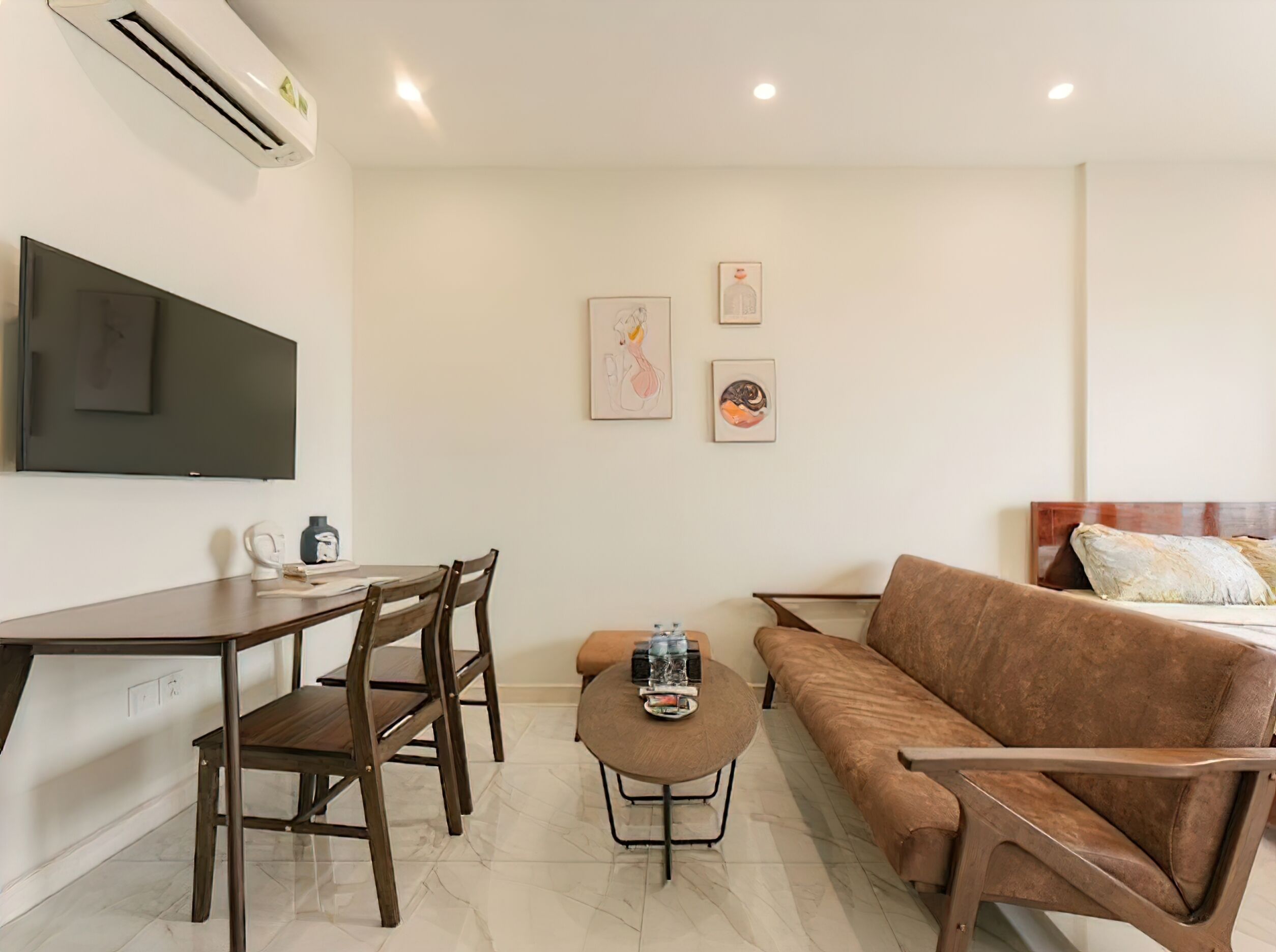 Una habitación moderna y bien iluminada con un televisor de pantalla plana, un sofá marrón, una mesa de comedor con sillas y una pequeña mesa de centro.