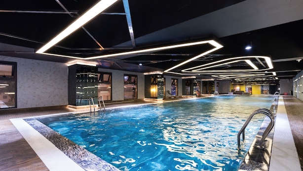 Una piscina interna con luci moderne, zona piscina limpida e area relax con posti a sedere e un bar.
