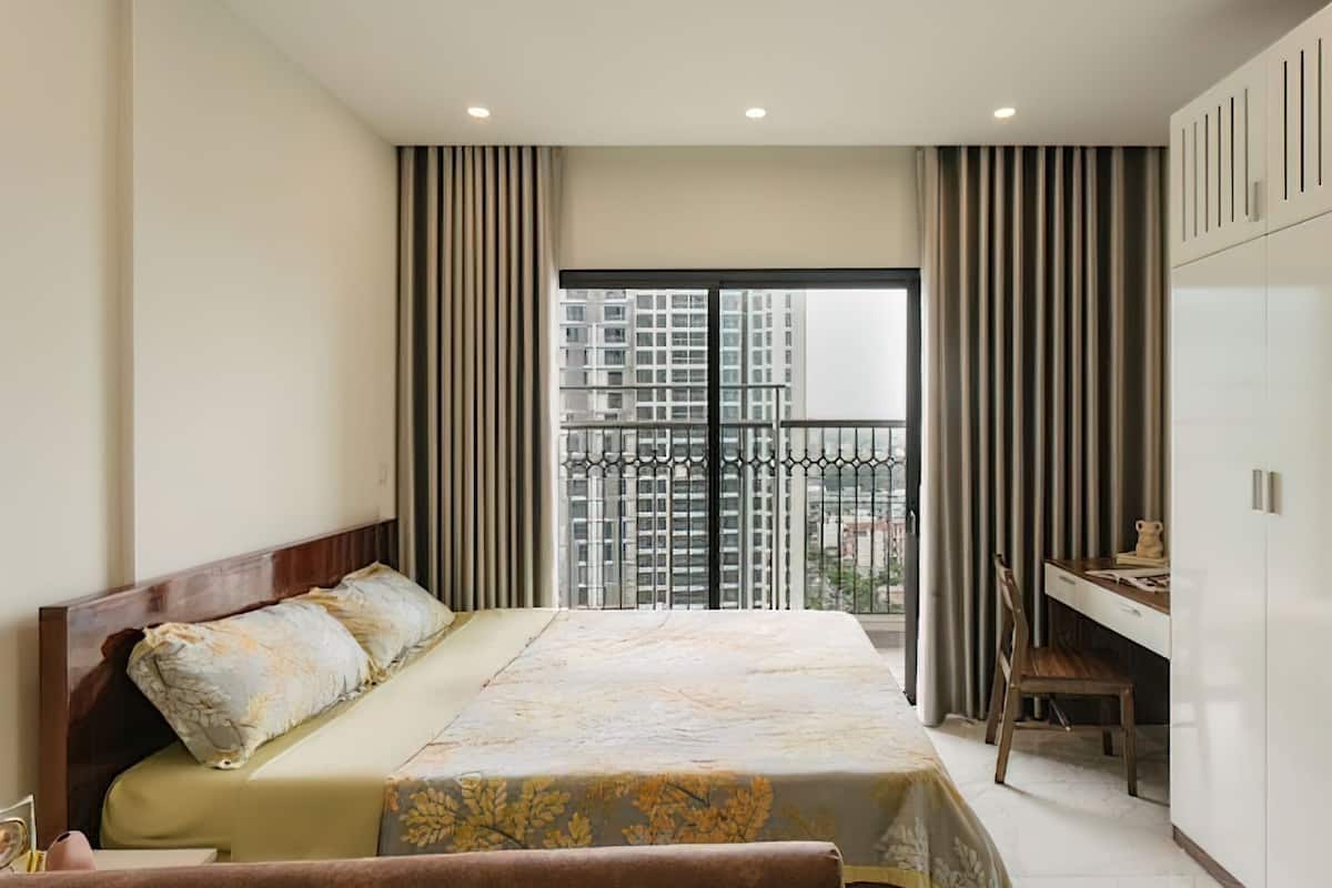 Un dormitorio con una cama grande, un escritorio y vistas a rascacielos desde un balcón.