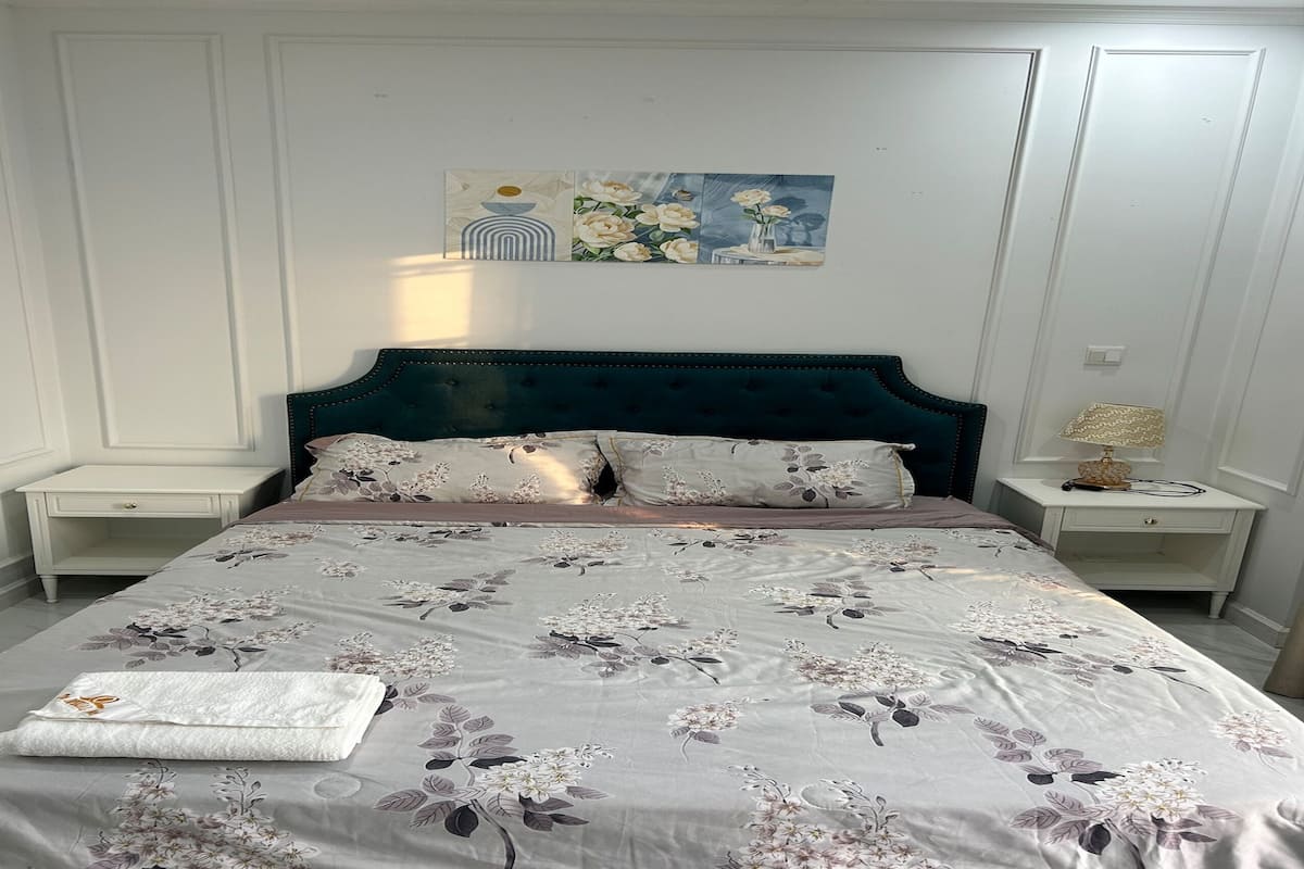 Una cama bien hecha con ropa de cama floral, un cabecero oscuro y una mesita de noche con una lámpara.
