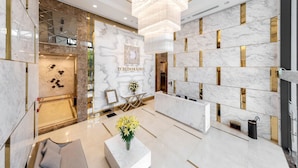 Un'elegante hall d'albergo moderna con pareti in marmo, una reception e un lampadario.
