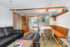 Un salon avec un canapé, une table à manger entourée de chaises, un banc en bois et, au fond, un coin cuisine.