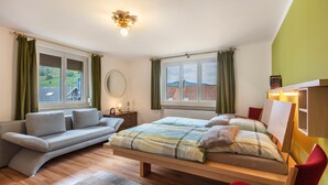 A bedroom with a bed, a sofa, a red chair, and two windows. - Apartment '95qm, 2 Schlafräume' with Mountain View, Shared Terrace and Wi-Fi (Todtnau)