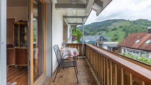 A balcony with a wooden railing, a table with chairs, and a view of a green hillside. - Apartment '95qm, 2 Schlafräume' with Mountain View, Shared Terrace and Wi-Fi (Todtnau)