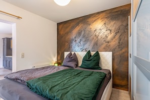 Un dormitorio con cama, almohadas, cabecera y una pared con textura.