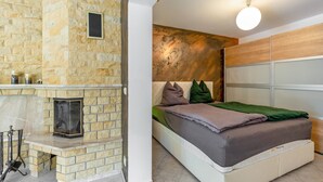 Une chambre avec une cheminée en pierre, un lit avec des oreillers, une tête de lit et un luminaire fixé au mur.