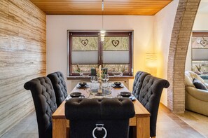 Een eethoek met een houten tafel, zwarte stoelen met bekleding en een raam met hartvormige decoraties.