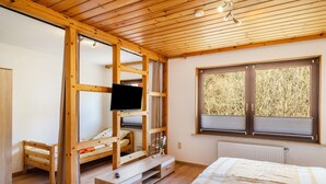 Ein Zimmer mit Holzrahmen, das ein Bett, einen Fernseher und ein Fenster mit Blick auf Bäume bietet.