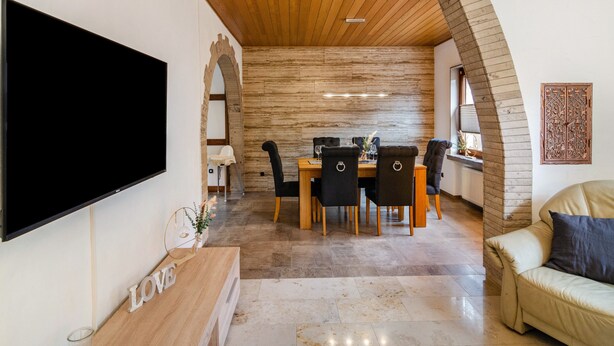 Ein modernes Wohnzimmer mit Flachbildfernseher, einem Essbereich mit Holztisch und Stühlen sowie einer gemütlichen Sitzecke mit einer Couch.