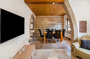 Een moderne woonkamer met een flatscreen televisie, een eethoek met een houten tafel en stoelen, en een gezellige zithoek met een bank.