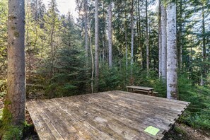 A wooden deck in a forest with tall trees and a picnic table. - Trekking Camp on the Renchtalsteig – Campsite (Oppenau)