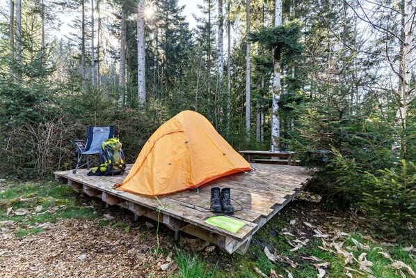 A camping setup with a tent on a wooden platform, a chair, and a backpack.