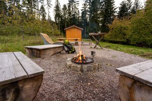 A campfire with benches, a wooden structure, and a forested background.