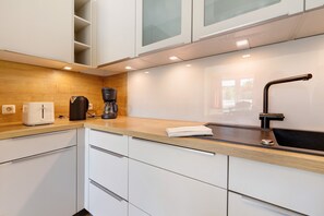 Une cuisine moderne avec des meubles blancs, un plan de travail en bois, une machine à café et un évier.