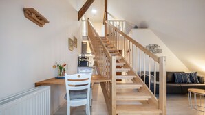 Eine Treppe führt zu einer oberen Etage, ein Essbereich mit Tisch und Stühlen sowie ein Sofa in einem Wohnraum.