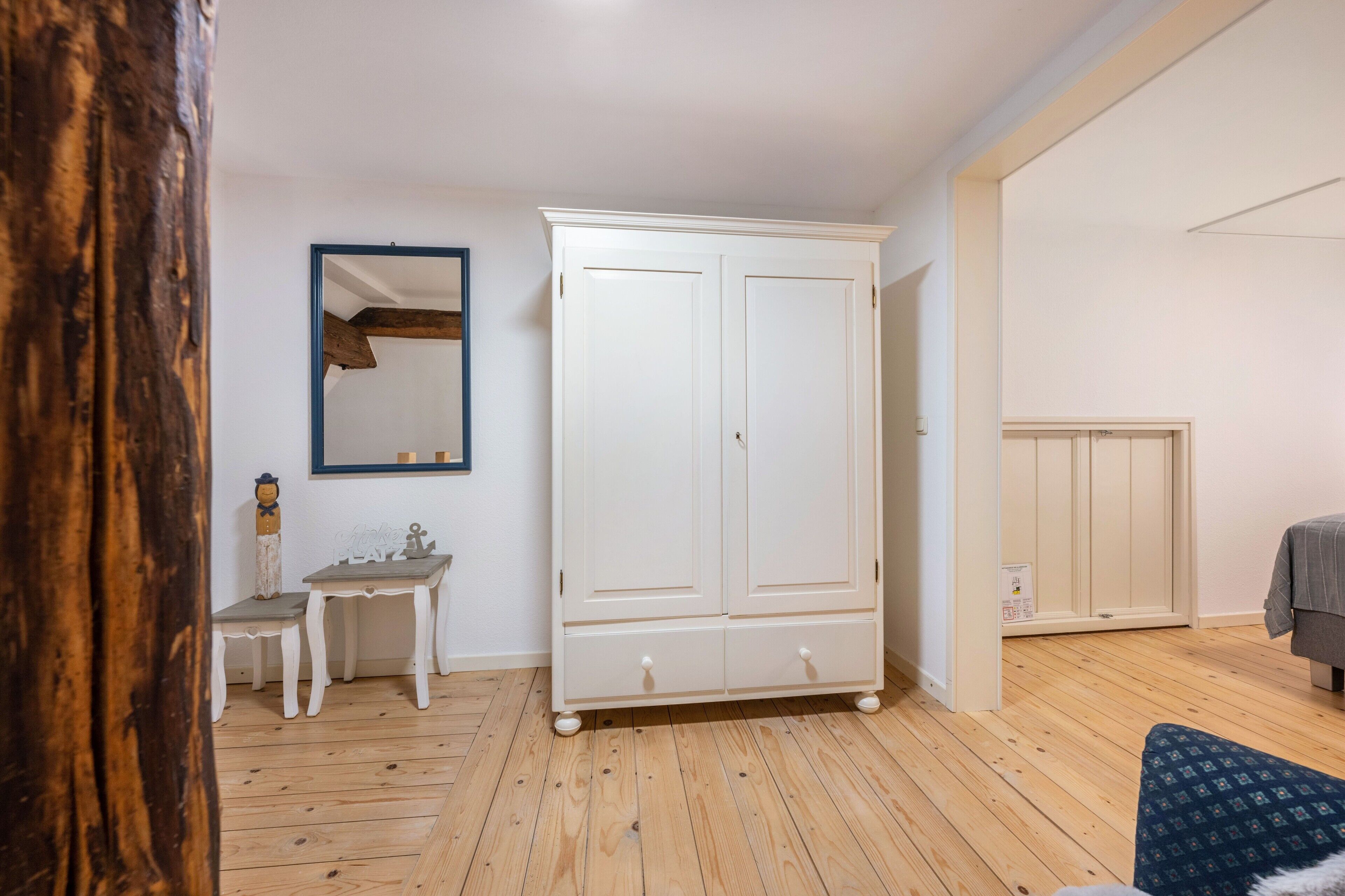 Une pièce avec un plancher en bois, une armoire blanche, une petite table et un miroir au mur.