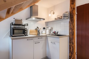 A kitchen with white cabinets, a microwave, a toaster, a coffee maker, and a wooden beam ceiling.