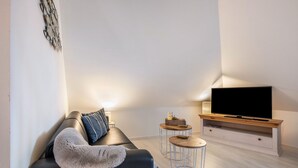 Ein modernes Wohnzimmer mit einer Couch, zwei Beistelltischen, einem Fernseher und einer Wanddekoration.